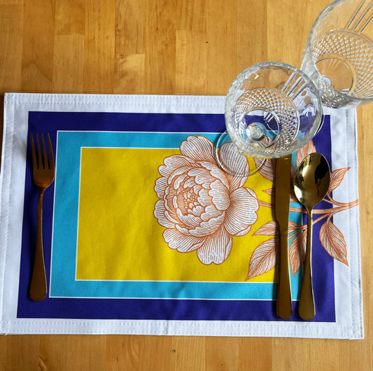Placemat with peony design on a wooden table with golden cutlery and glasses.